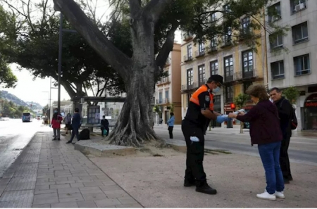 Un miembro de Protección Civil entrega mascarillas a pasajeros de autobuses (ÁLEX ZEA/EUROPA PRES)