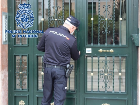 Un agente comprueba el estado de la puerta de acceso a un bloque en la que ha sido forzada la cerradura (POLICÍA NACIONAL) 